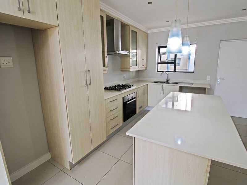 Modern kitchen featuring light wood cabinetry, stone countertops, a central island, and integrated appliances including a gas hob and oven.