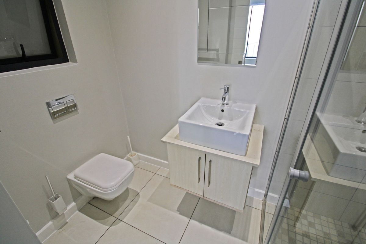 Modern bathroom featuring a wall-mounted toilet, vanity cabinet with vessel sink, and a glass-enclosed shower with tiled flooring.