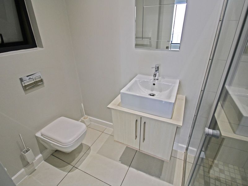 Modern bathroom featuring a wall-mounted toilet, vanity cabinet with vessel sink, and a glass-enclosed shower with tiled flooring.