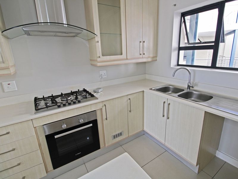 Modern kitchen featuring light wood cabinetry, stone countertops, a gas hob, built-in oven, extractor fan, and a double bowl stainless steel sink.