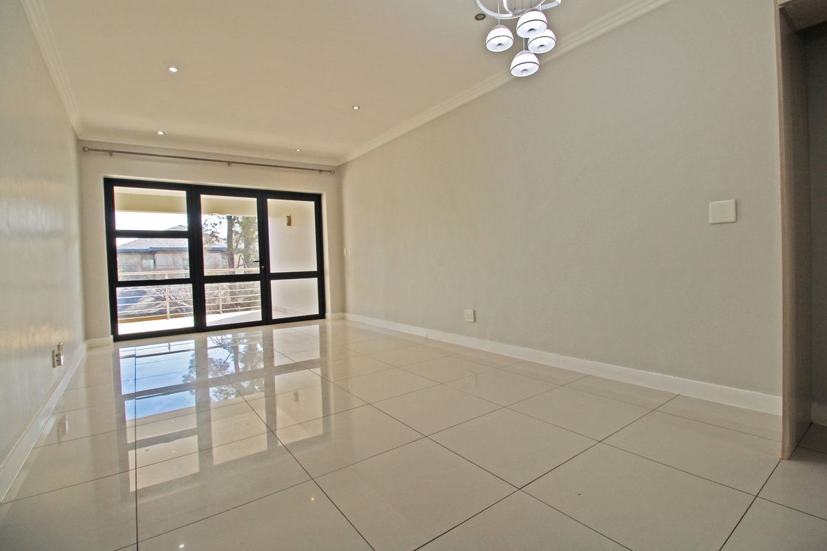 A bright, empty living room featuring polished porcelain floor tiles, recessed downlights, a modern chandelier, and a large sliding glass door leading to a balcony.