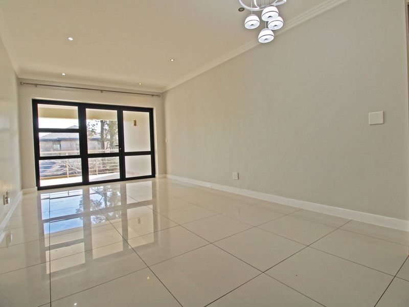 A bright, empty living room featuring polished porcelain floor tiles, recessed downlights, a modern chandelier, and a large sliding glass door leading to a balcony.