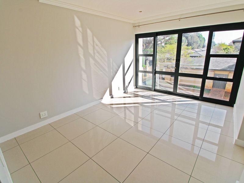 A bright, empty living area featuring large format tiled flooring and expansive black aluminium sliding doors that provide ample natural light.