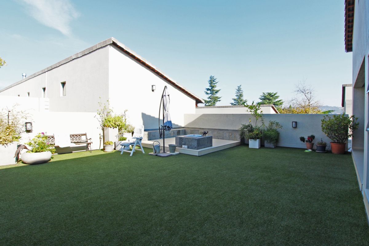 A private rear garden featuring artificial turf, a raised tiled patio area, and perimeter boundary walls.