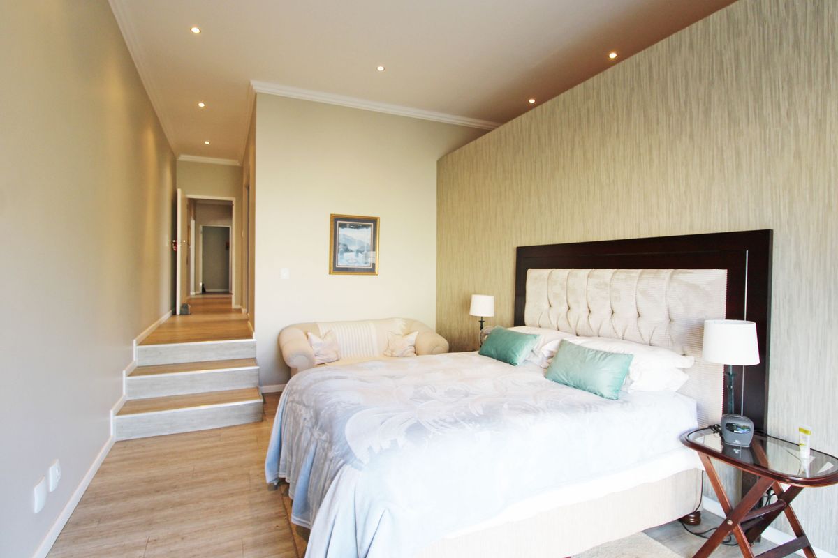 Spacious bedroom featuring a raised floor level, recessed ceiling lighting, and a textured feature wall, leading into a connecting hallway.