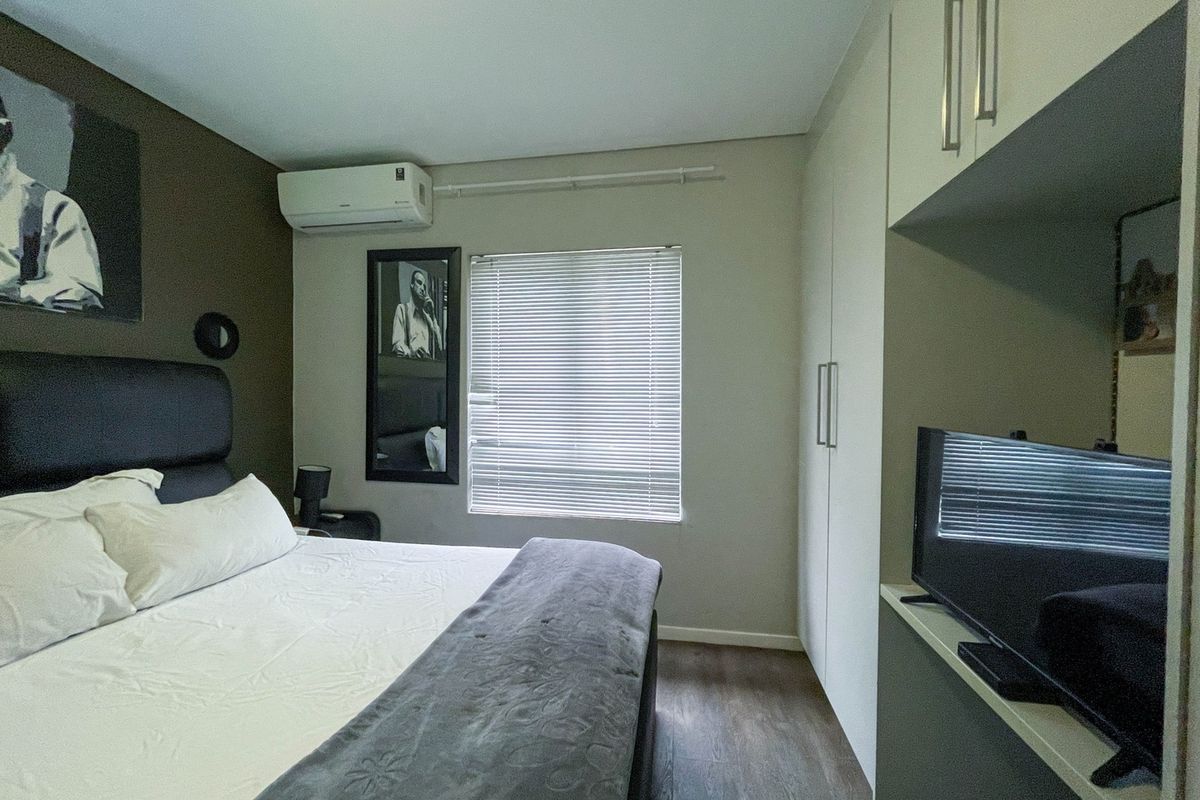 A well-maintained bedroom featuring built-in cupboards, a wall-mounted air conditioning unit, and wood-look flooring.