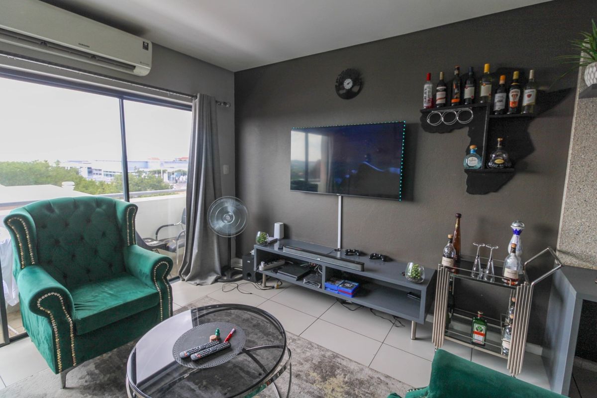 A living room featuring tiled flooring, a wall-mounted television, and a split-system air conditioning unit, with direct access to an outdoor balcony.