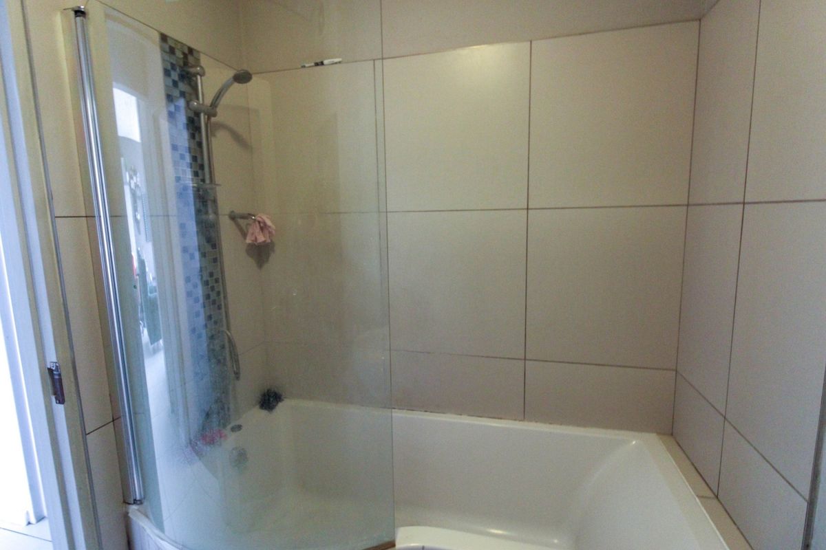 A functional bathroom featuring a built-in bathtub with a glass shower screen and a wall-mounted shower head with decorative mosaic tile accents.