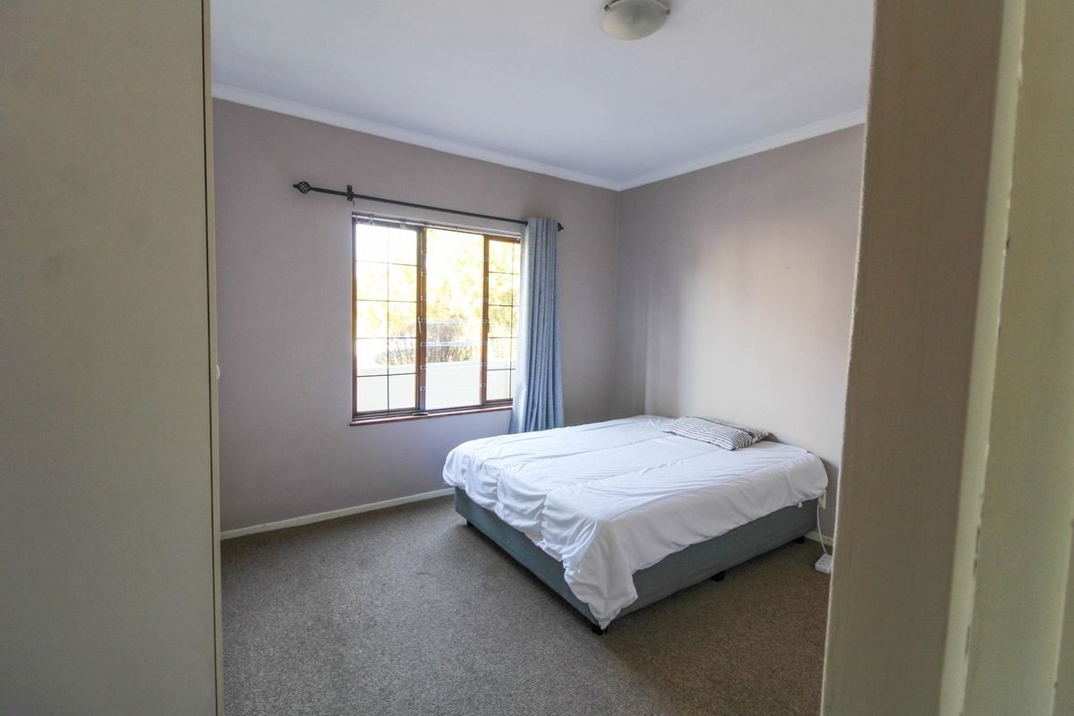 A standard bedroom featuring neutral wall tones, carpeted flooring, and a window with a curtain rod.