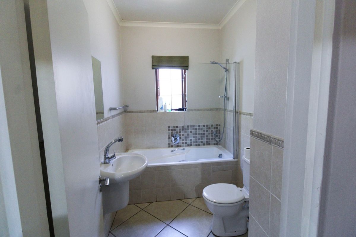 A functional bathroom featuring a pedestal basin, a combined bathtub and shower with a glass screen, and neutral wall tiling.