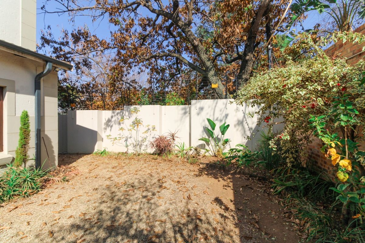 A private rear garden area featuring a perimeter boundary wall and established landscaping, offering a quiet outdoor space for the apartment.