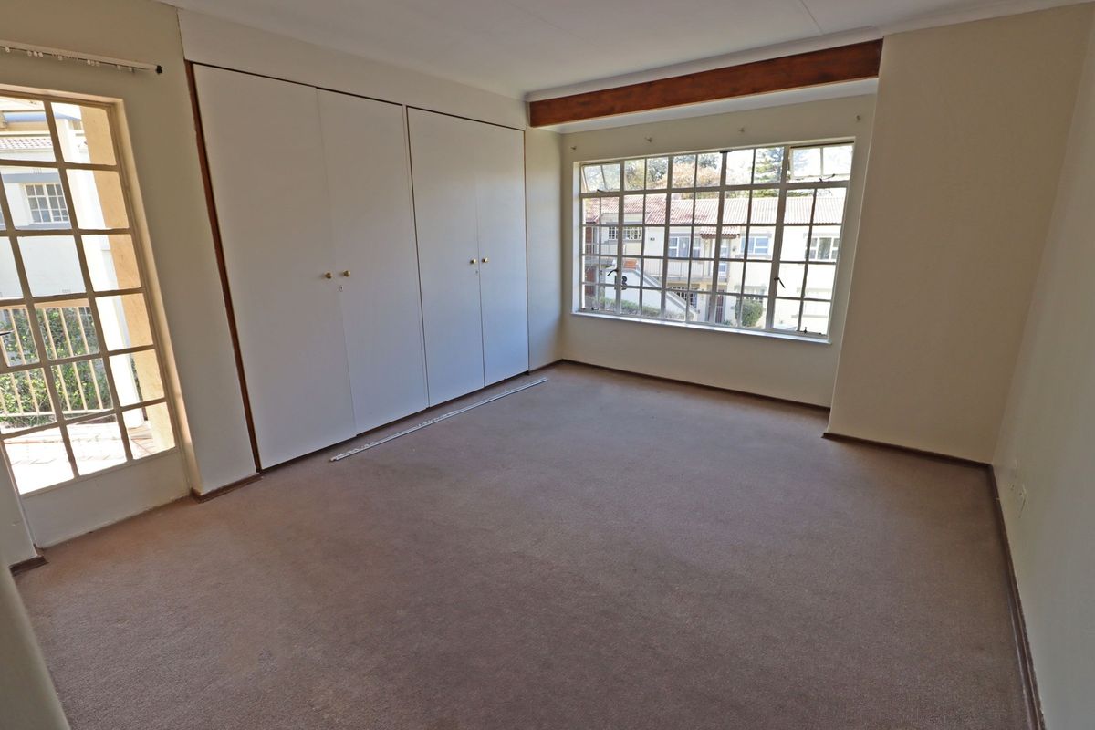 A spacious, empty bedroom featuring built-in cupboards, large windows, and direct access to a balcony area.