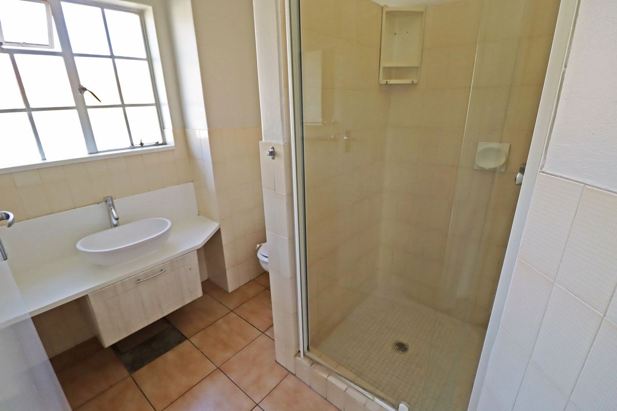 A functional bathroom featuring a glass-enclosed shower, a modern vessel sink vanity, and tiled flooring with natural light from a window.