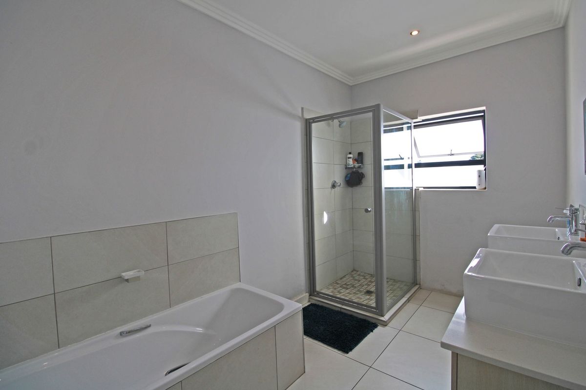 A modern bathroom featuring a built-in bathtub, a separate glass-enclosed shower, and a double vanity setup with tiled flooring.