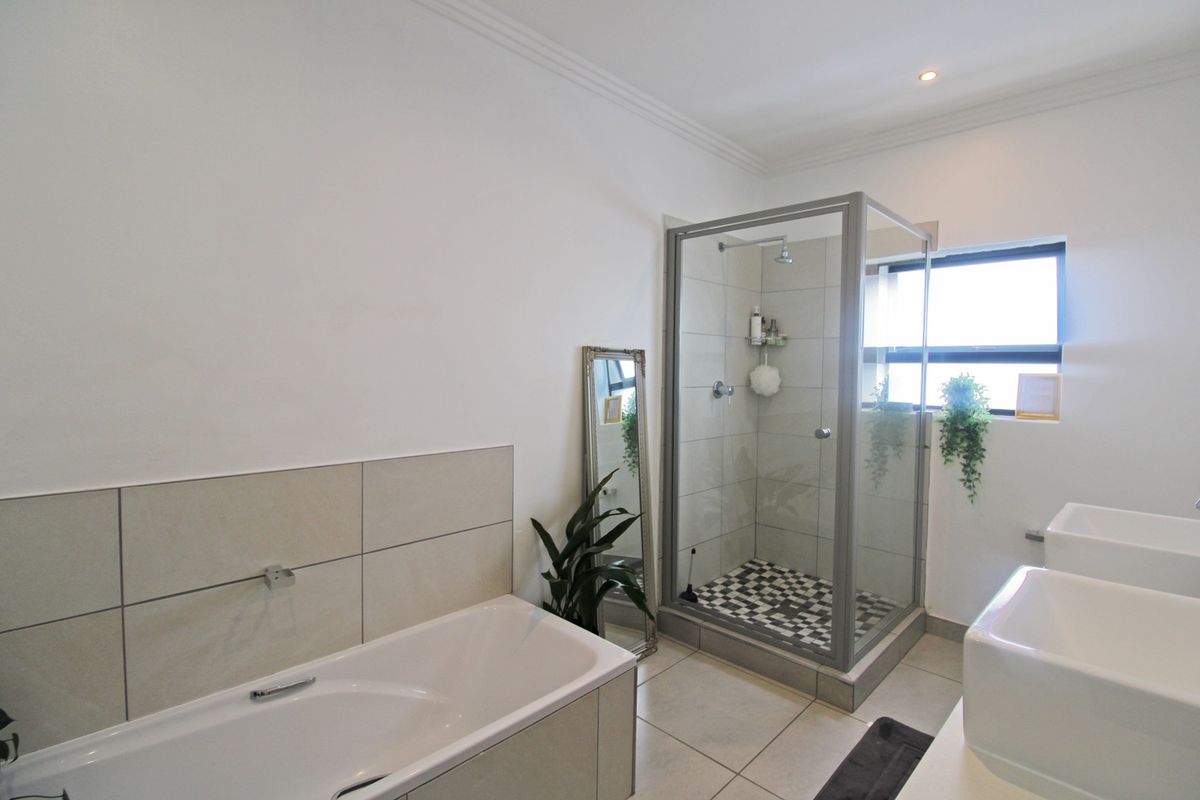 Modern bathroom featuring a built-in bathtub, separate glass-enclosed shower, and double vanity sinks with neutral tiling throughout.