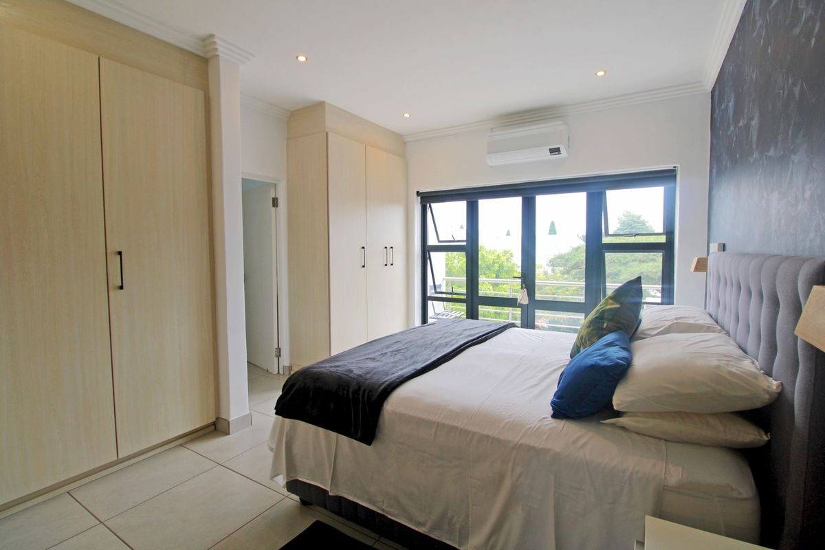 A well-maintained bedroom featuring built-in cupboards, tiled flooring, recessed lighting, and an air conditioning unit with access to a balcony.