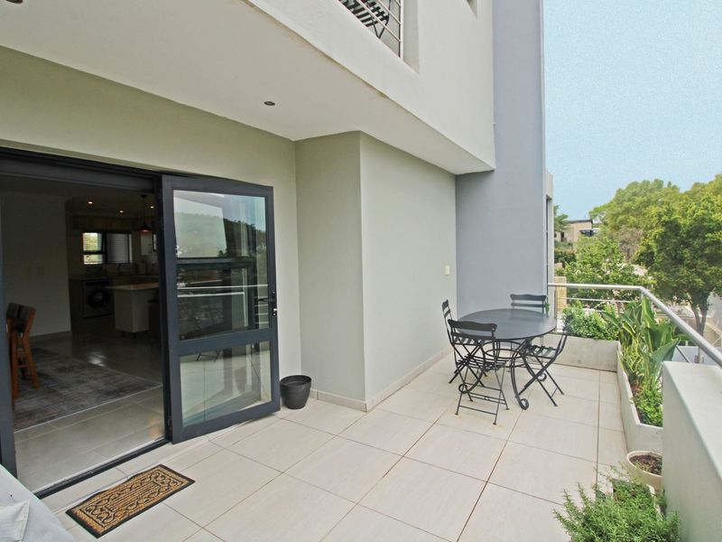 A spacious covered balcony featuring tiled flooring, a metal balustrade, and built-in planter boxes, providing seamless indoor-outdoor flow through large sliding glass doors.