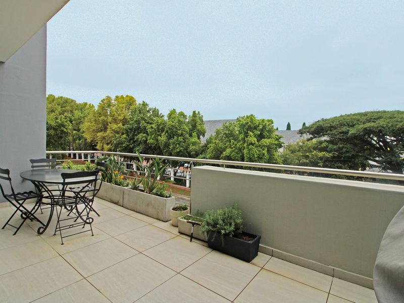 A spacious balcony featuring tiled flooring, a metal balustrade, and built-in planter boxes, offering a pleasant outdoor area with elevated views.