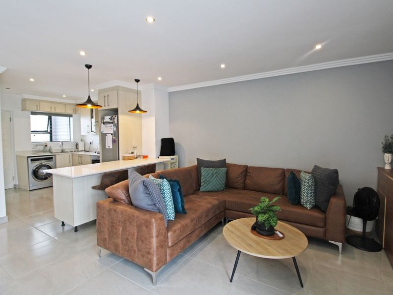 Open-plan living area featuring a modern kitchen with stone countertops, built-in cabinetry, and recessed lighting, seamlessly flowing into the lounge space.