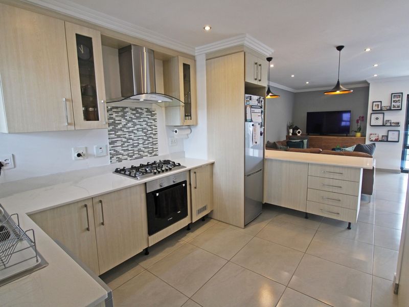 Modern open-plan kitchen featuring light wood cabinetry, stone countertops, gas hob, and integrated appliances, flowing seamlessly into the adjacent living area.