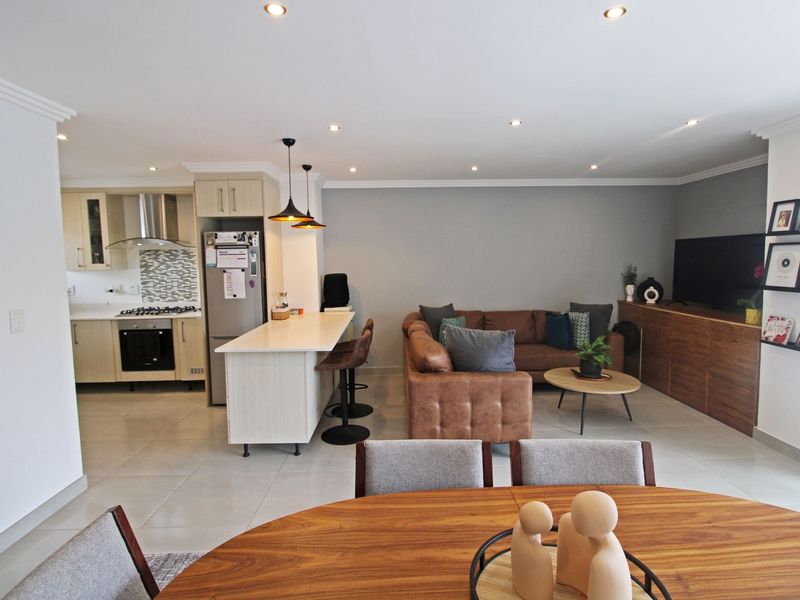 An open-plan living area featuring a modern kitchen with built-in appliances, a central island, and a spacious lounge area with tiled flooring throughout.
