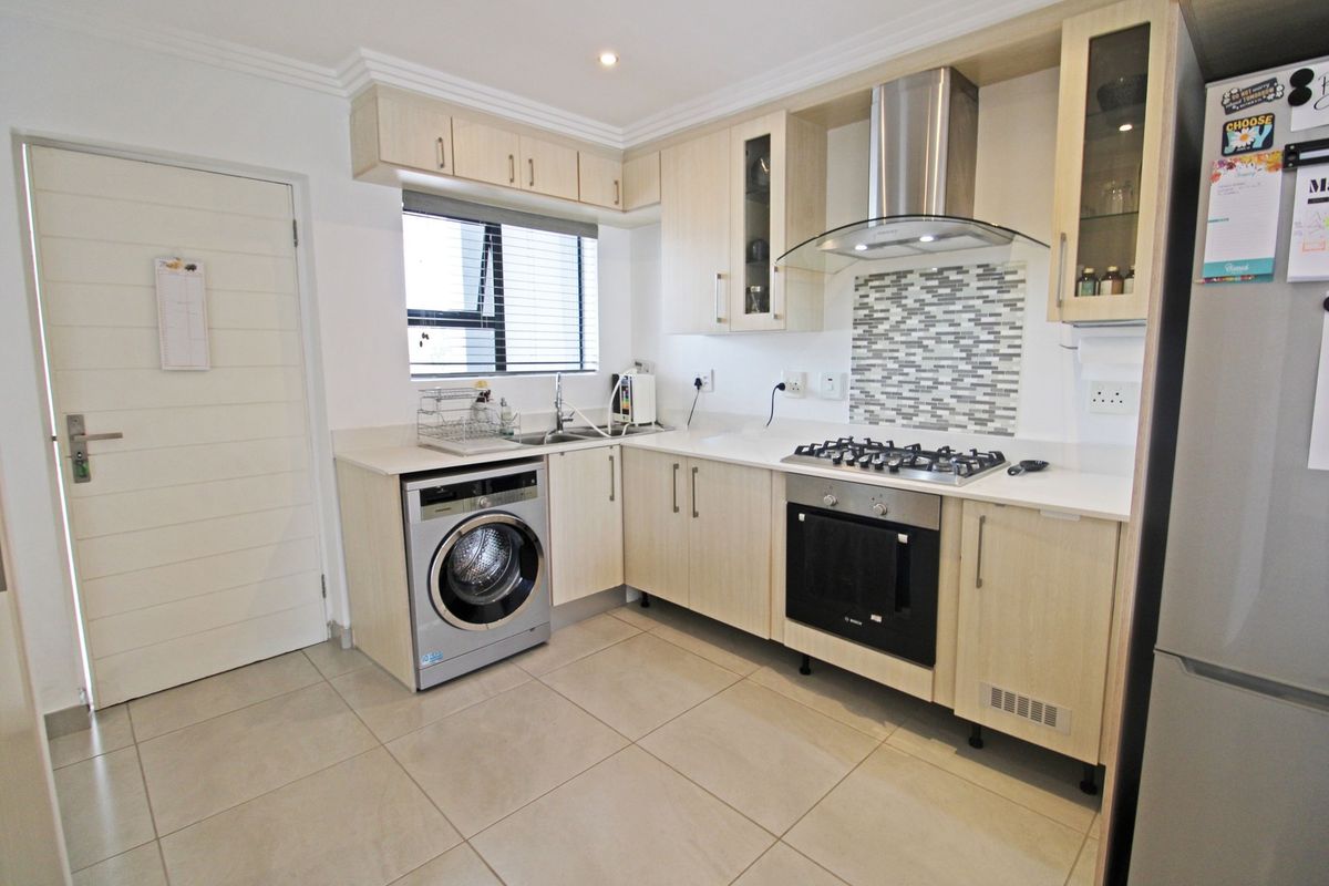 Modern kitchen featuring light wood cabinetry, stone countertops, mosaic splashback, gas hob, electric oven, extractor fan, and a built-in washing machine.