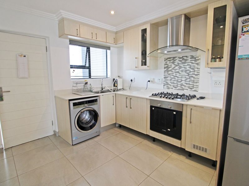 Modern kitchen featuring light wood cabinetry, stone countertops, mosaic splashback, gas hob, electric oven, extractor fan, and a built-in washing machine.