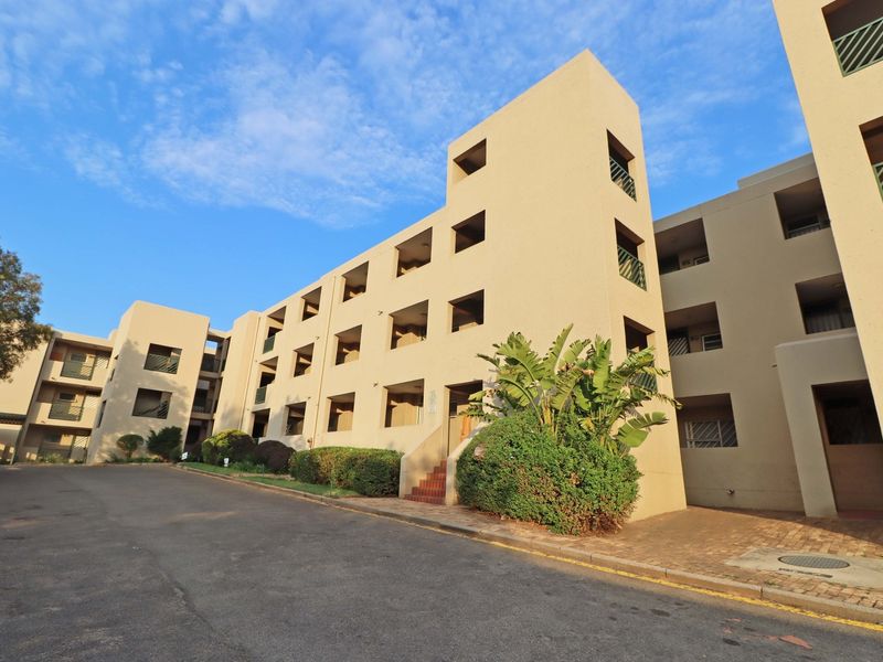 Exterior view of a multi-story apartment complex featuring paved driveway access, balconies, and established garden landscaping.