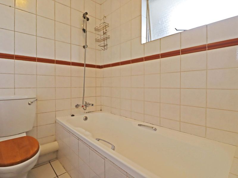 A functional bathroom featuring a bathtub with shower mixer, toilet, and tiled wall finishes with a decorative border.