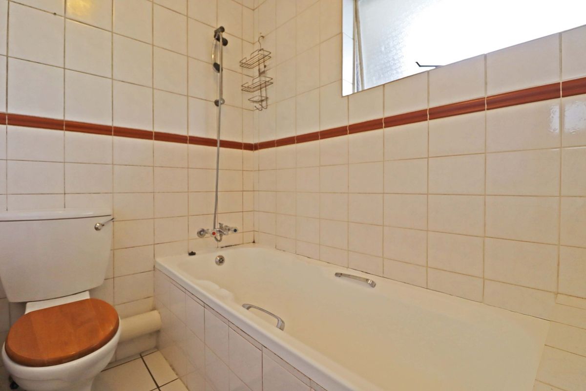 A functional bathroom featuring a bathtub with shower mixer, toilet, and tiled wall finishes with a decorative border.