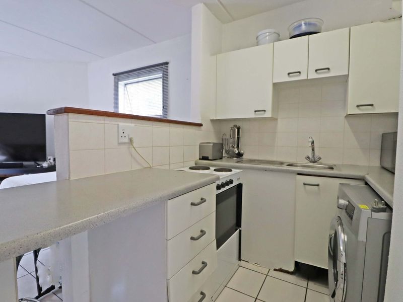 Compact open-plan kitchen featuring white cabinetry, laminate countertops, electric stove, and tiled flooring, integrated with the adjacent living area.