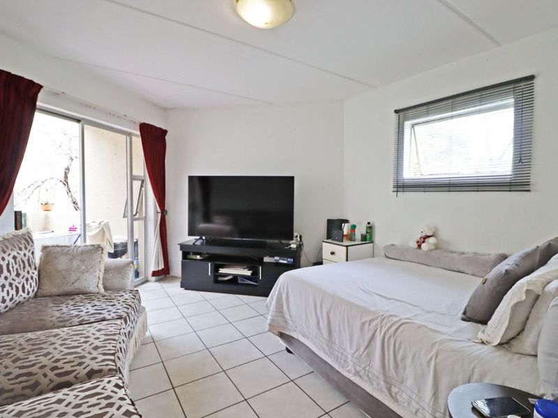 A functional bedroom featuring tiled flooring, a sliding glass door providing access to an outdoor area, and an awning window for natural light.