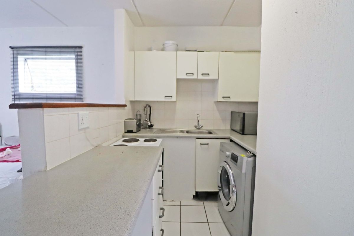 Compact kitchen featuring built-in cabinetry, laminate countertops, a stainless steel sink, and an electric hob, with tiled flooring and backsplash.