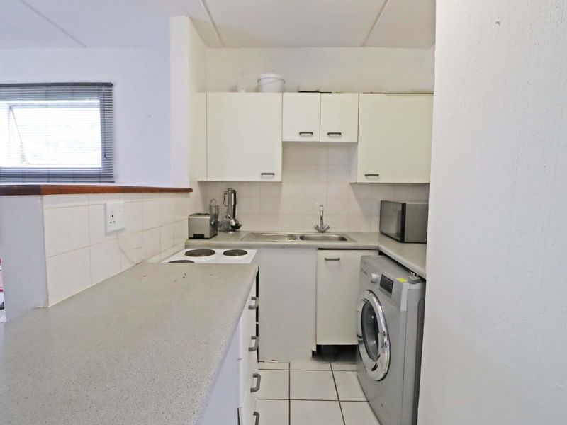 Compact kitchen featuring built-in cabinetry, laminate countertops, a stainless steel sink, and an electric hob, with tiled flooring and backsplash.