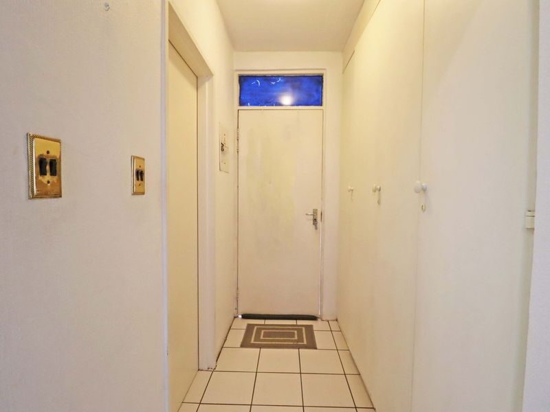 A narrow hallway featuring tiled flooring, built-in storage cupboards, and a transom window above the door, providing a functional transition space within the apartment.