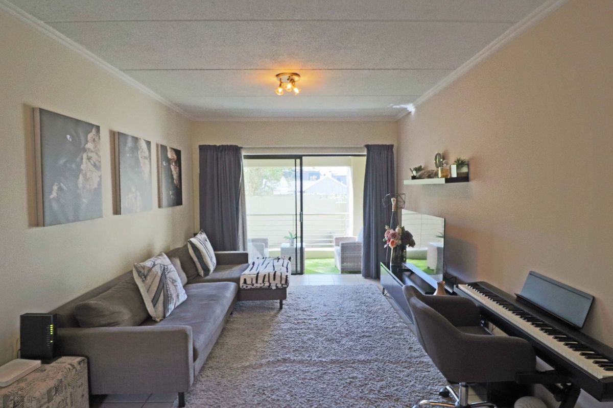 A well-maintained living room featuring tiled flooring, coved ceilings, and a large sliding glass door providing access to an outdoor balcony area.