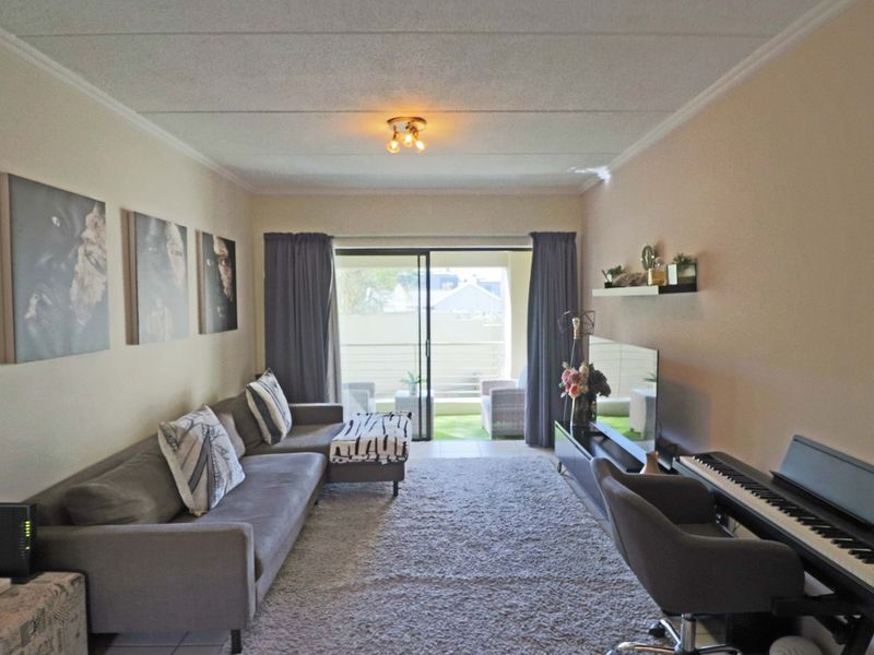 A well-maintained living room featuring tiled flooring, coved ceilings, and a large sliding glass door providing access to an outdoor balcony area.
