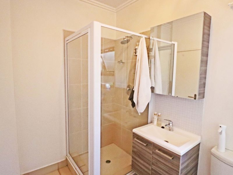A functional bathroom featuring a glass shower enclosure, modern vanity with basin, mirror cabinet, and toilet with neutral tiled finishes.