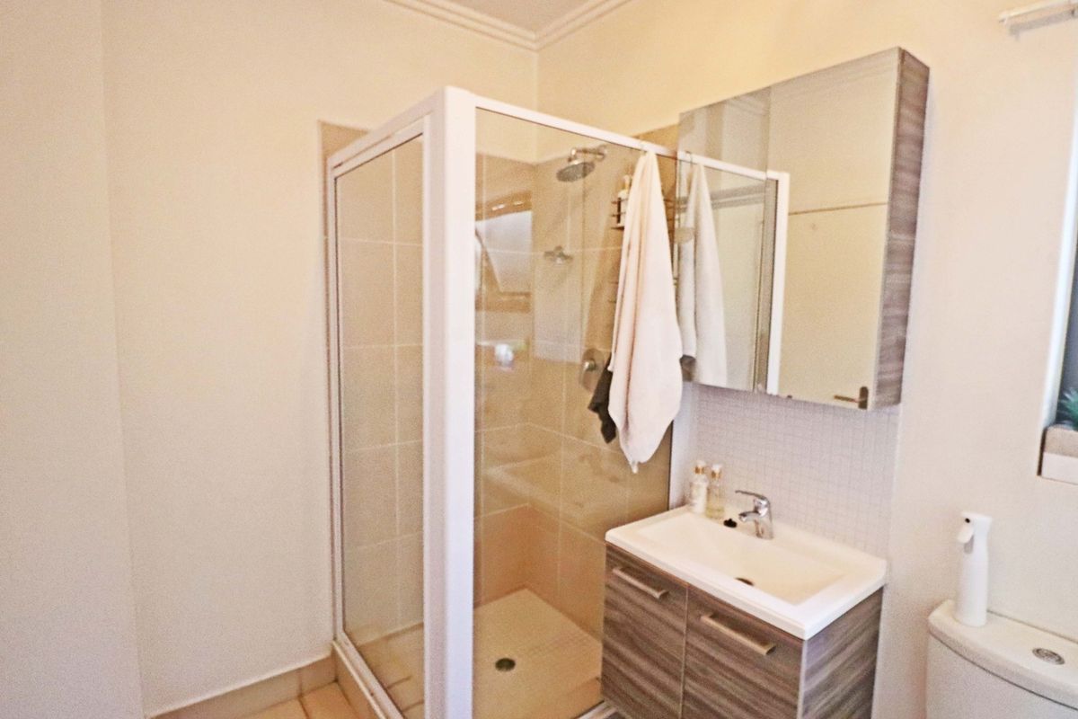 A functional bathroom featuring a glass shower enclosure, modern vanity with basin, mirror cabinet, and toilet with neutral tiled finishes.