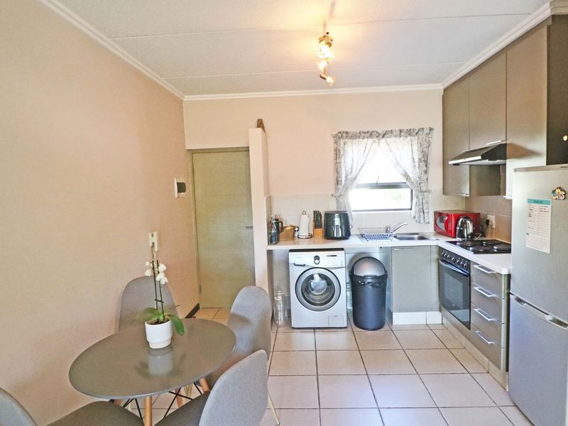 A functional kitchen featuring built-in cabinetry, integrated oven and hob, extractor fan, and dedicated space for a washing machine with tiled flooring throughout.