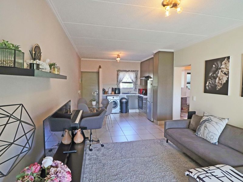 Open-plan living area featuring a compact kitchen with built-in cabinetry, oven, and hob, seamlessly flowing into the lounge space with tiled flooring throughout.