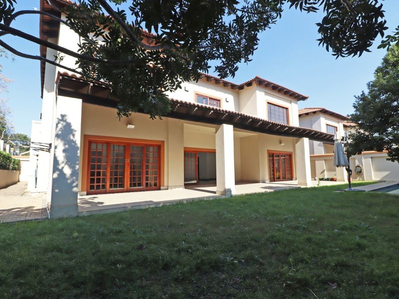 Rear view of a two-story house featuring a spacious covered patio with timber rafters, wooden sliding doors, and access to a garden and swimming pool.