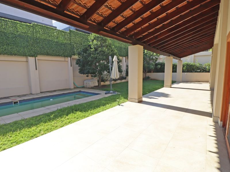 Covered patio area featuring a timber pergola, tiled flooring, and direct access to a swimming pool and garden space.
