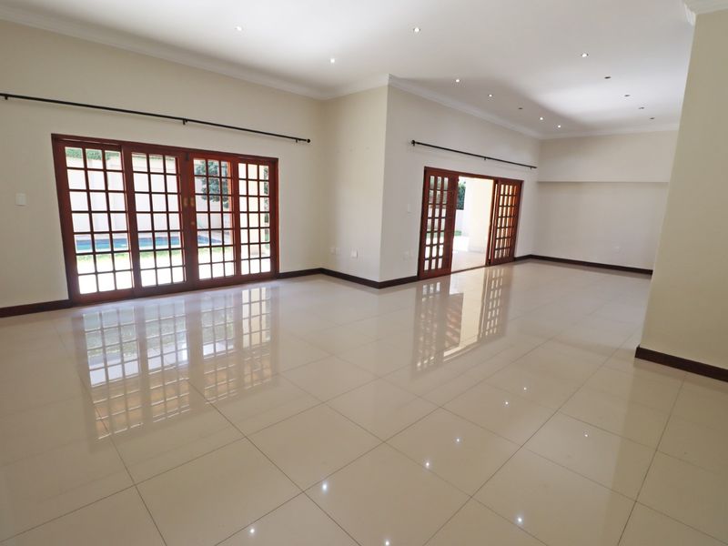 Spacious, light-filled living area featuring polished porcelain tiles, recessed downlighting, and multiple sets of wooden french doors opening to the garden.