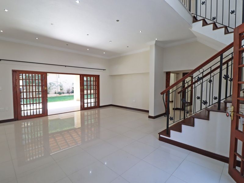 Spacious, light-filled living area featuring polished porcelain tiles, recessed lighting, and a feature wooden staircase with wrought iron detailing, opening onto the garden.