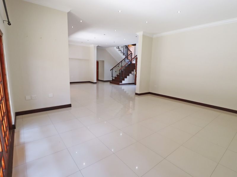Spacious, open-plan living area featuring polished tile flooring, recessed lighting, and a prominent staircase with a decorative wrought iron balustrade.