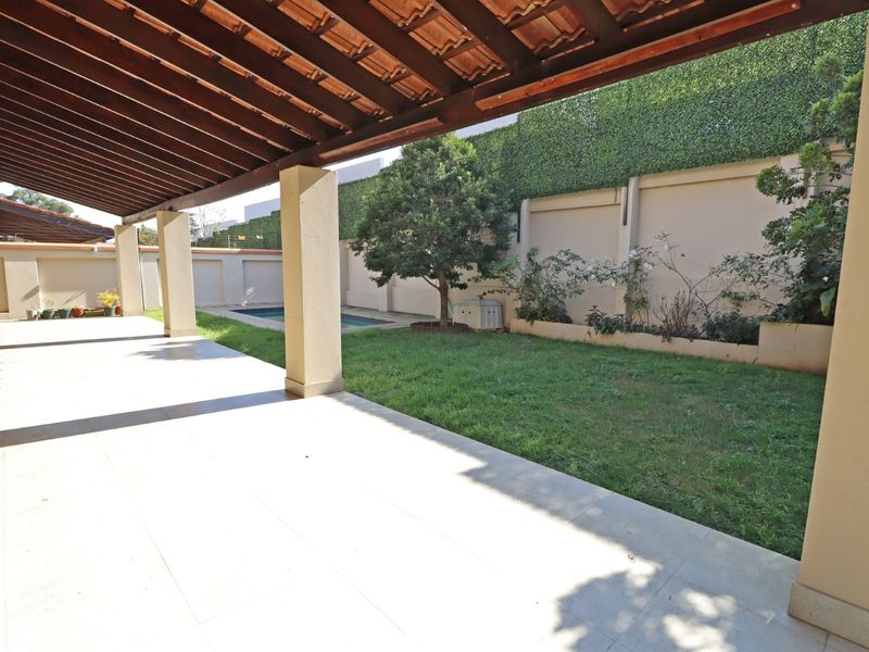 A spacious covered patio featuring a timber pergola, overlooking a private garden with a swimming pool and high boundary walls.