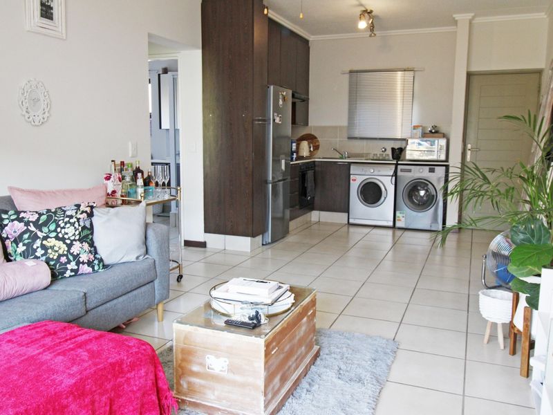 Open-plan living area featuring a compact kitchen with dark cabinetry, tiled flooring, and integrated laundry appliances, creating a functional and connected living space.