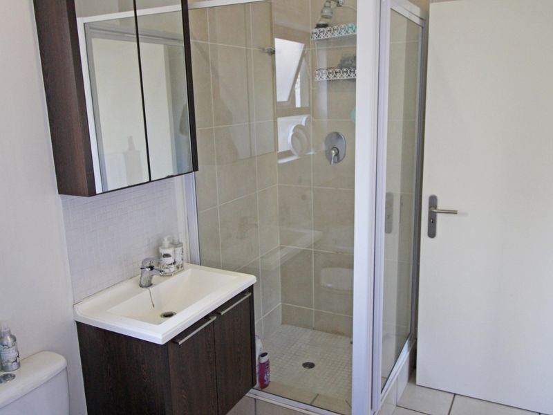 A functional bathroom featuring a vanity with basin, medicine cabinet, and a glass-enclosed shower with tiled finishes.