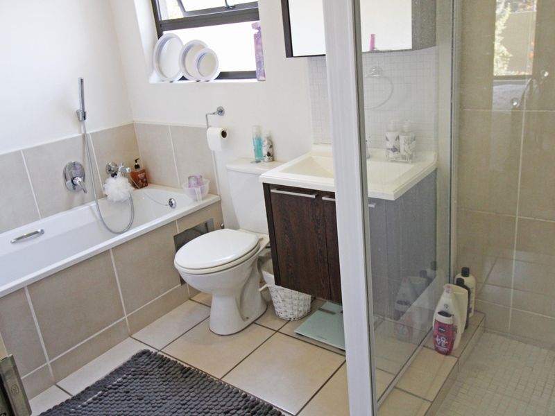 A functional bathroom featuring a built-in bathtub, separate shower enclosure, vanity cabinet, and toilet with neutral wall and floor tiling.